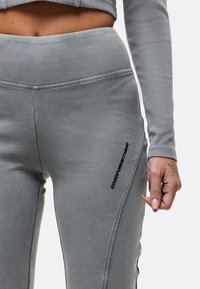 Grijze geribde leggings met een hoge tailleband. Kenmerken zijn zwarte zijbranding en contrasterende stiksels, die de textuur en pasvorm benadrukken.