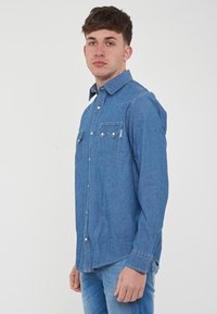 Camicia in denim blu con colletto a punta, chiusura con bottoni e due tasche sul petto. Presenta uno stile western classico con tessuto testurizzato.