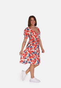 Bloemenjurk in rood, blauw en wit met pofmouwen en een smocktail. In combinatie met witte sneakers heeft het een knielange, vloeiende zoom.