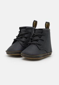 Botas de tornozelo em couro preto com uma textura suave, bico redondo e costura amarela na sola. Possui atacadores e alças para facilitar o calçar.