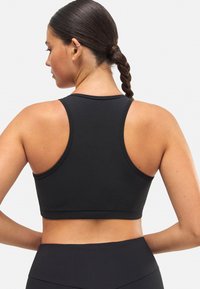 Sujeción deportiva negra con diseño tipo corredor, fabricada en tejido liso y elástico. Presenta costuras planas y una silueta ajustada.