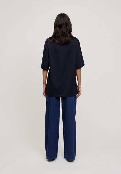 T-shirt oversize navy à manches courtes, fabriqué à partir d'un tissu doux. Associé à un pantalon en denim à jambes larges, mettant en valeur une coupe décontractée.