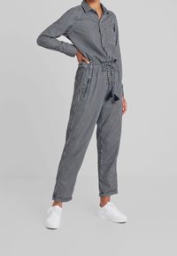 Randig jumpsuit med knapp-up överdel, långa ärmar och knytmidja. Har två sidofickor och en bröstficka, tillverkad av lättviktig tyg.