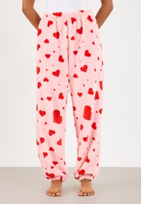 Fleece teplákové nohavice v svetloružovej farbe s roztrúsenými červenými srdci. Obsahujú elastický pás a manžety na lemoch pre pohodlné nosenie.