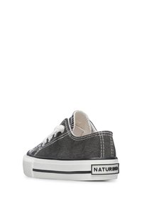 Czarne trampki na płaskiej podeszwie z białymi sznurowadłami, białą gumową podeszwą, czarnymi paskami ozdobnymi oraz naszywką z logo na pięcie. Teksturowana cholewka z kontrastowym szwem.