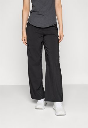 Black, wide-leg pants made from lightweight fabric. Features an elastic waistband and smooth texture, paired with white athletic shoes.