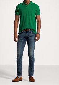 Grön pikétröja med korta ärmar, blå logodetalj, i kombination med jeans i medelblå tvätt och bruna mockaskor. Ett brunt bälte fulländar outfiten.