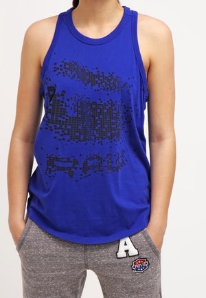 Canotta blu con design grafico pixelato nero, scollatura rotonda e materiale in cotone morbido. Abbinata a pantaloni della tuta grigi con un patch a forma di "A".