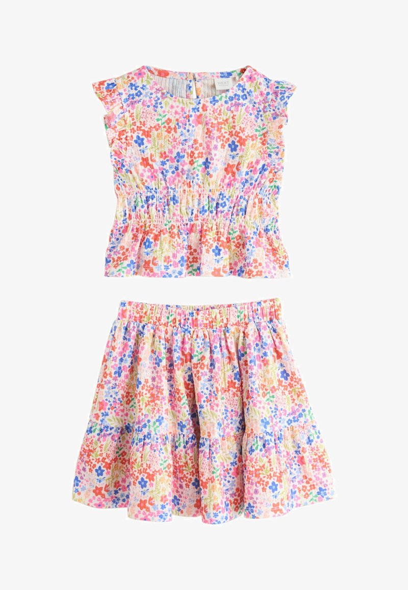 Ensemble deux pièces fleuri composé d'un haut à corsage froncé et d'une jupe à volants. Fond rose clair orné de fleurs multicolores et manches à volants.