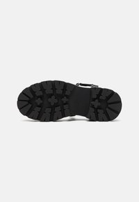 Black rubber shoe sole with deep tread patterns and traction grooves. Features a smooth central section with reinforcement around the edges.