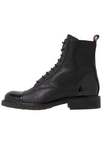 Bota de tobillo de cuero negro con un acabado texturizado, puntera redondeada y cordones en la parte frontal. Presenta una puntera brillante y un tirador en la parte trasera.