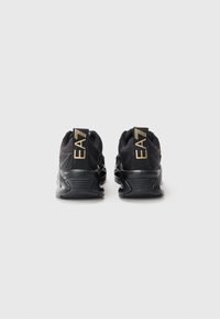 Pair of black athletic shoes with thick soles viewed from the back on a white background, featuring gold "EA7" branding on heel tabs.