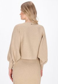 Beige geribde trui met ballonmouwen, cropped ontwerp en subtiele stiksels. Soepele textuur, minimalistische stijl en geen zichtbare hardware.