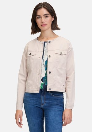 Light pink jacket with a round neckline, front buttons, and two chest pockets, paired with a patterned top and blue jeans.