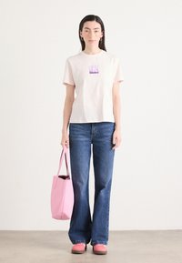 T-shirt in cotone rosa chiaro con una grafica quadrata viola, abbinata a jeans svasati blu, borsa a tracolla rosa e scarpe rosa. Design minimalista.
