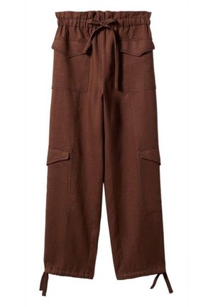 Mujer con suéter negro corto acanalado con botones, pantalones cargo marrones de cintura alta con lazos en los tobillos y sandalias negras de punta abierta, de pie.