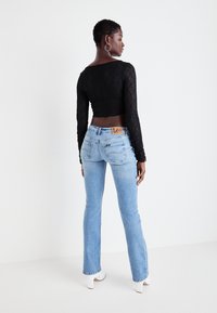 Zwarte cropped kanten top met lange mouwen, gecombineerd met lichtblauwe flare jeans met een logo label op de achterkant van de taille. Witte haklaarzen.