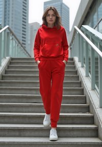 Rød sweatshirt med en frontlomme og matchende joggers, lavet af blødt stof, parret med hvide sneakers, på betonstrapper.