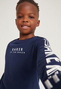 Marineblaues Langarmshirt mit "BAKER" in Weiß auf der Brust und dem Ärmel gedruckt. Weicher Stoff, Rundhalsausschnitt und bequemer Schnitt.