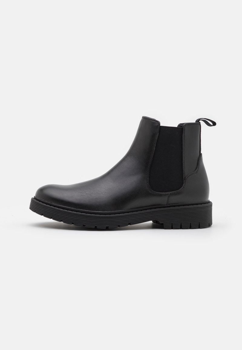 Botte Chelsea en cuir noir avec panneaux latéraux élastiques, languette à l'arrière et semelle épaisse rainurée sur fond blanc.