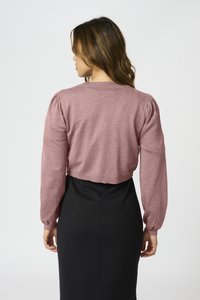 Pink cropped sweater with long puff sleeves, knitted texture, and a round neckline, paired with a black fitted skirt.