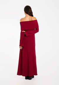 Robe rouge longue, décolletée sur les épaules, avec de longues manches évasées et un ourlet long jusqu'au sol. Tissu doux avec une texture lisse.