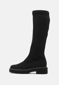 Bota negra hasta la rodilla hecha de material suave y elástico. Cuenta con una suela gruesa y texturizada y un sutil detalle de costura alrededor del borde.