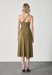 Robe côtelée vert olive avec un bustier ajusté, une jupe évasée et deux fines bretelles. Portée avec des sandales à talons noires.