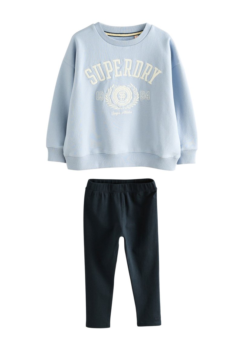 Šviesiai mėlynas medvilninis džemperis su „SUPERDRY“ logotipu ir herbu kreminės spalvos, derinamas su juodos spalvos tamprėmis tamprėmis. Kasdienis, laisvo silueto derinys.