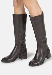 Bottes en cuir marron à hauteur de genou avec un talon carré, dotées d'une fermeture éclair sur le côté et d'une texture lisse. Le design comprend un tige ajustée et un bout arrondi.