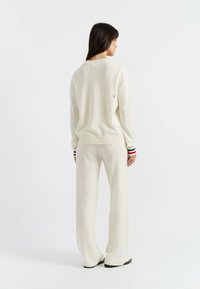 Beige gebreide trui met ribgebreide manchetten en rode, witte en blauwe strepen, gecombineerd met bijpassende beige wide-leg broeken. Eenvoudig logo detail op de achterkant.