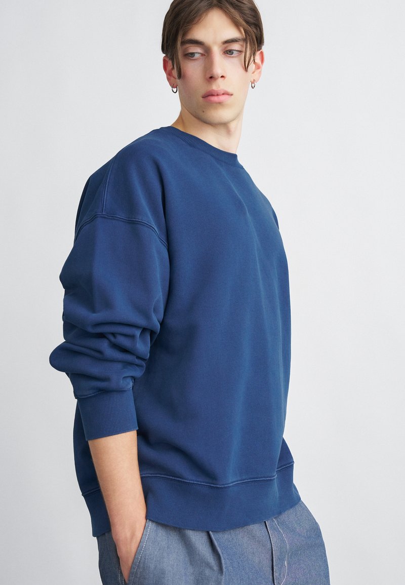 Marineblaue Sweatshirt aus Baumwollmischung, mit Rundhalsausschnitt, überschnittenen Schultern und gerippten Bündchen. Glatte Textur mit minimalen Details.