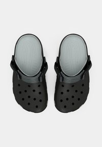 Czarne gumowe chodaki z otworami wentylacyjnymi, szarą wkładką i regulowanymi paskami na piętę zapewniającymi pewne dopasowanie. Strukturalna powierzchnia dla lepszej przyczepności.