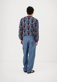 Pulover cu model circular multicolor, bază albastră deschisă. Pantaloni cargo din denim, largi, cu multiple buzunare. Sandale negre cu dungi albe.