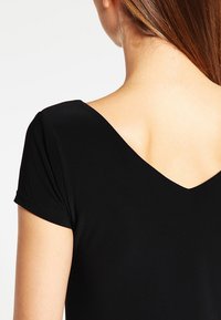 Haut noir à col en V avec un design ajusté, des manches courtes et une texture lisse, affichant une esthétique minimaliste et moderne.