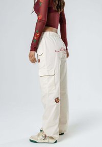 Pantalones cargo beige con bordados de flores, con un ajuste holgado y cinturilla elástica, combinados con zapatillas blancas con estampados.