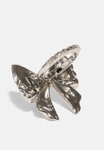 Il portan ring in argento a forma di farfalla presenta una finitura metallica lucida, con un anello posizionato sopra intricati dettagli floreali.