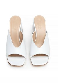 Mule sandal in pelle bianca con punta aperta e tacco a blocco, con solette beige decorate con il nome del marchio, fotografate dall'alto su uno sfondo bianco.