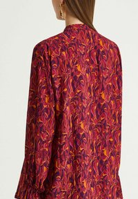 Bluse mit floralem Druck in lebendigem Pink, Orange und Lila. Verfügt über lange Ärmel mit gerafften Bündchen und eine lockere Passform. Rückansicht gezeigt.