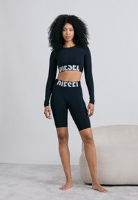 Czarny krótki top z długim rękawem oraz dopasowane, wysokowciskane krótkie spodenki rowerowe z białym logo "DIESEL". Przylegający fason, gładki materiał, minimalistyczny design.