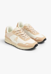Beige und weiße Sneaker mit einem strukturierten Wildleder- und glatten Leder-Obermaterial, featuring einem Schädel-Logo und einer schwarzen Gummisohle.