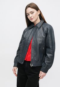 Zwarte leren jas met een gladde textuur, ritssluiting, geribbelde manchetten en een kraag, gedragen over een rode trui.