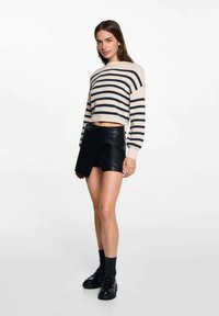 Maglione corto a righe beige e blu navy con maniche lunghe, abbinato a una mini gonna avvolgente in ecopelle nera. Scarpe nere con lacci e calzini grigi.