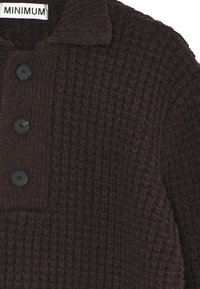 Barna kötött pulóver texturált mintázattal, galléros nyakkivágással és három fekete gombbal az elején. A címke felirata: "MINIMUM."