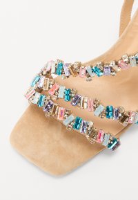 Beige semsket sandal med tre stropper dekorert med fargerike perler i rosa, blått og lilla, med en kvadratisk tådesign.