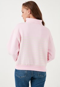 Felpa rosa con colletto alto e vestibilità rilassata, caratterizzata da strisce orizzontali grigio chiaro sul retro. Tessuto morbido e orlo a costine.