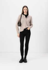 Ljusrosa stickad cardigan med knappar, svart turtleneck, svarta skinny jeans och svarta skor, tillsammans med en liten mörk handväska.