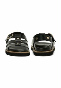 Sandalias de cuero negro con múltiples correas, acentos de hardware en forma circular y suela texturizada. Costura detallada a lo largo de los bordes.