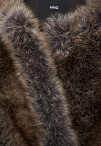 Brun faux fur tyg med en mjuk, fluffig textur och varierade nyanser. Har mörkare accenter och en subtil lyster på kanterna.