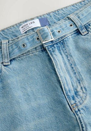 Light blue wide-leg jeans with a high-rise waist, featuring a silver buckle and two metal button closures at the front. Denim texture is visible.